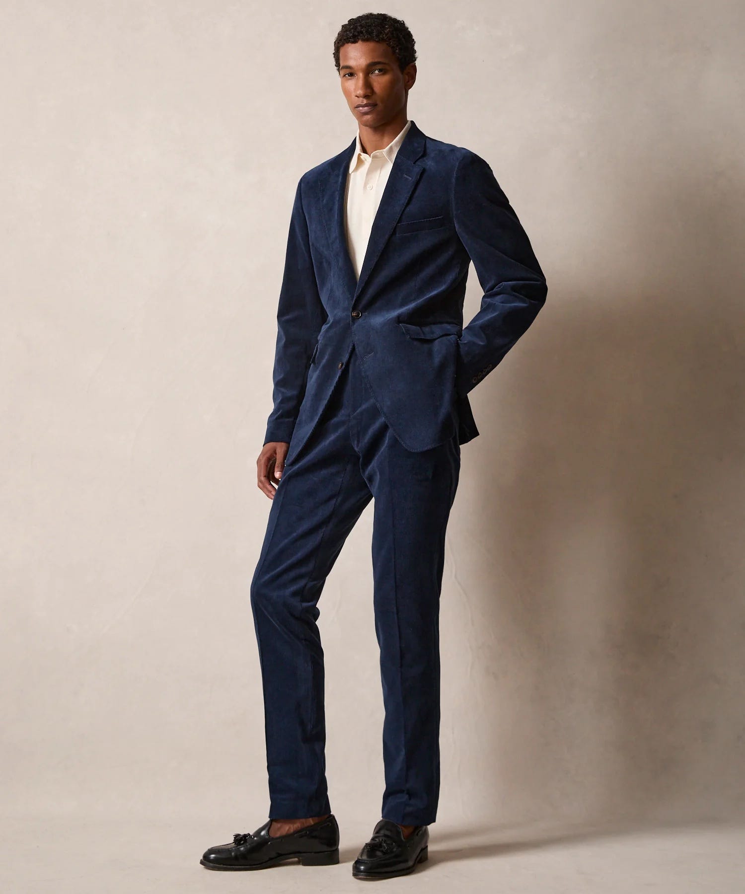 man wearing a navy corduroy suit with an off-white dress shirt and dark brown tassel loafers